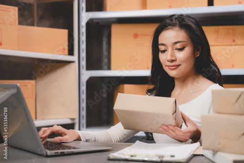 Asian woman e-business entrepreneur checking order and packing parcel box of product shipping delivery business, freelance marketing owner having online cyberspace to work with logistic package job