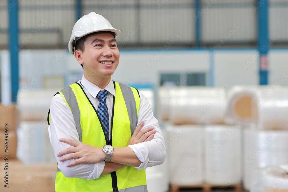 Asian engineering worker man portrait standing and arm crossed with happy smiling face with confident and blurred large warehouse background Asian engineering worker man portrait standing and arm crossed with happy smiling face with confident and blurred large warehouse background