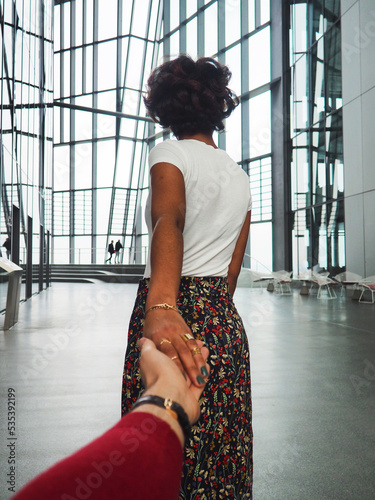 Back view of woman pulling someone's hand indoor