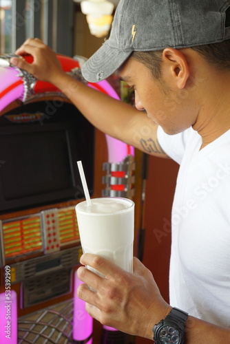 Man holding a cup of milkshake standing beside pink jukebox photo