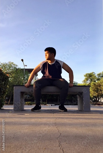 Man sitting on bench while glancing his right side surrounded with tall and green trees