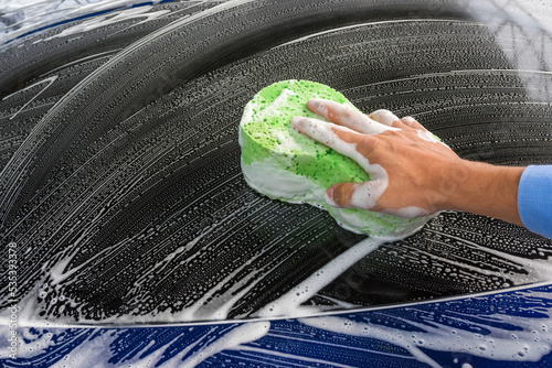 Person cleaning blue car with green sponge photo