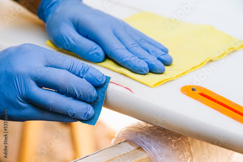 Surfer with protective gloves sanding a repair on the surfboard. photo