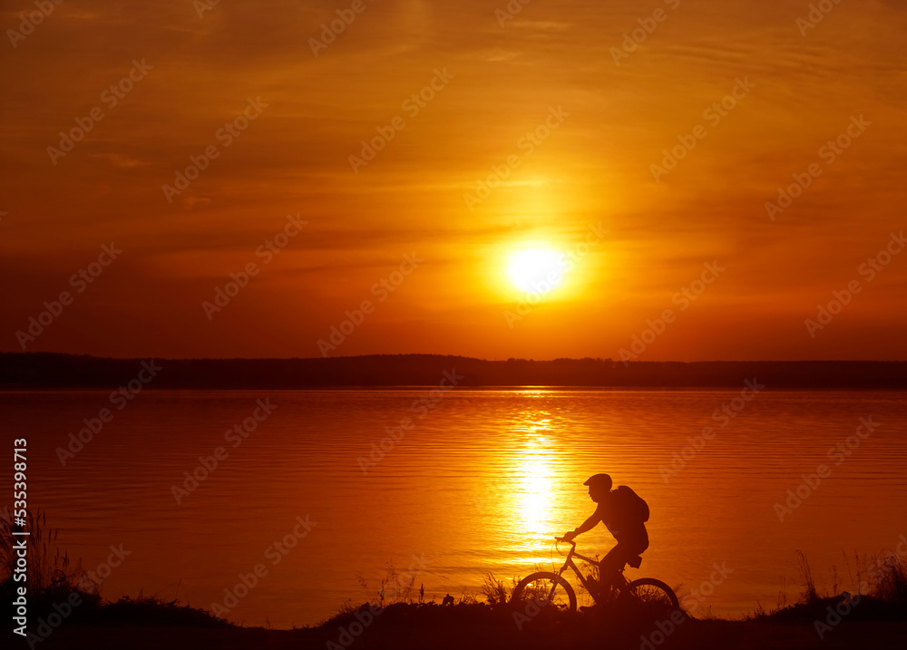 Image of sporty one tourist man walking along the shore with the bike against sunset sky with clouds and sun rays. alone woman. Silhouette race with high speed