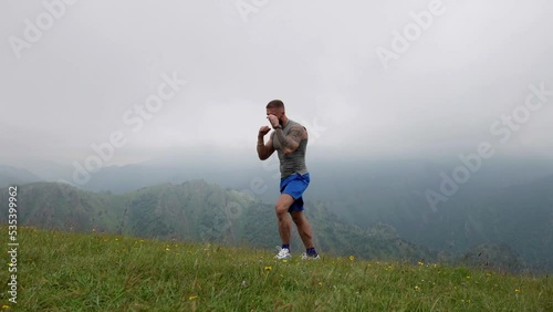 Athletic man is training and fighting in nature, handsome sporty man is boxing alone at top of mount