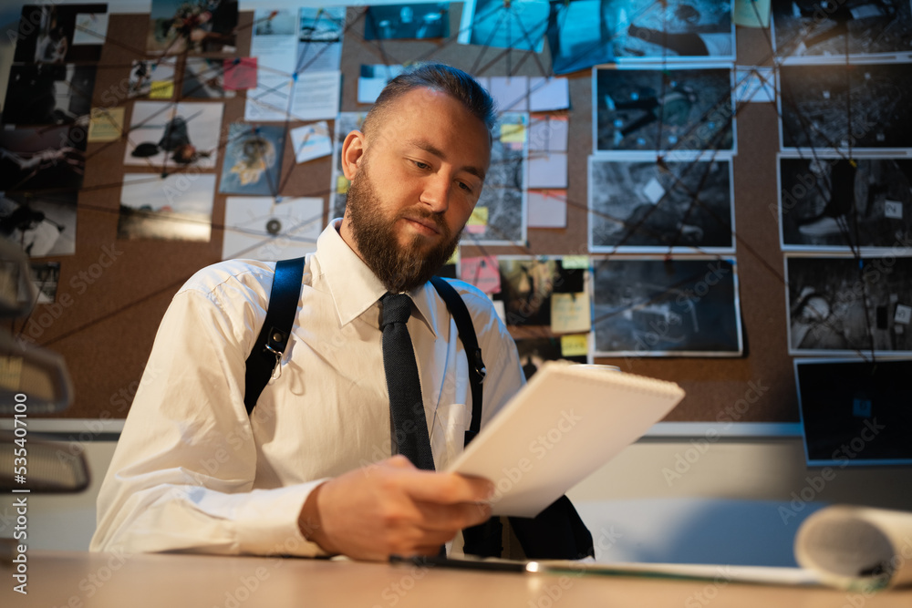 Detective working at desk in his office on workplace with documents while learning criminal profiles during investigation. Detective processing evidence