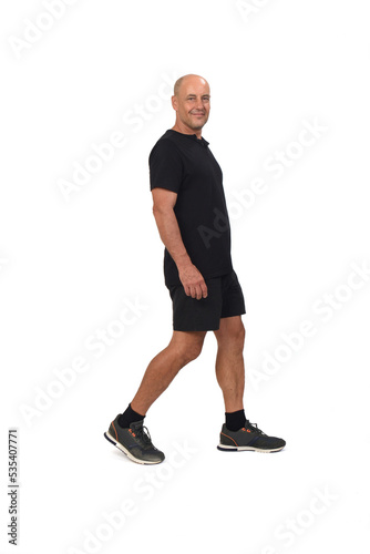 side view of a man with sportswear, t-shirt and shorts walking on white background, looking at camera