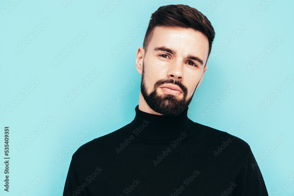 Handsome smiling model. Sexy stylish man dressed in black turtleneck sweater and jeans. Fashion hipster male posing near blue wall in studio. Isolated Handsome smiling model. Sexy stylish man dressed in black turtleneck sweater and jeans. Fashion hipster male posing near blue wall in studio. Isolated