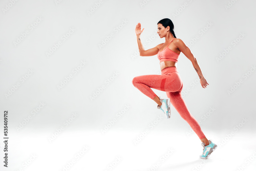 Fitness woman in sexy sports pink clothing. Young beautiful model with perfect body. Female posing in studio on grey background. Jumping and running. Jogging. Stretching before training. Isolated