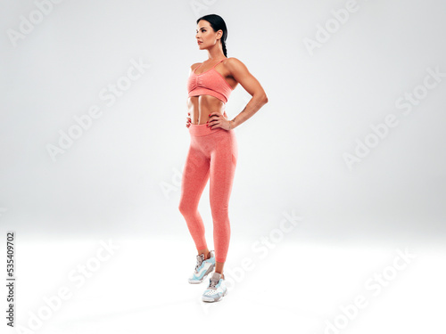Tanned fitness woman in pink sports clothing. Sexy young beautiful model with perfect body.Female isolated on grey background in studio. Stretching out before training