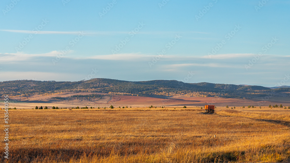 Obraz premium A truck drives along a country road in a field, with a mountain in the background