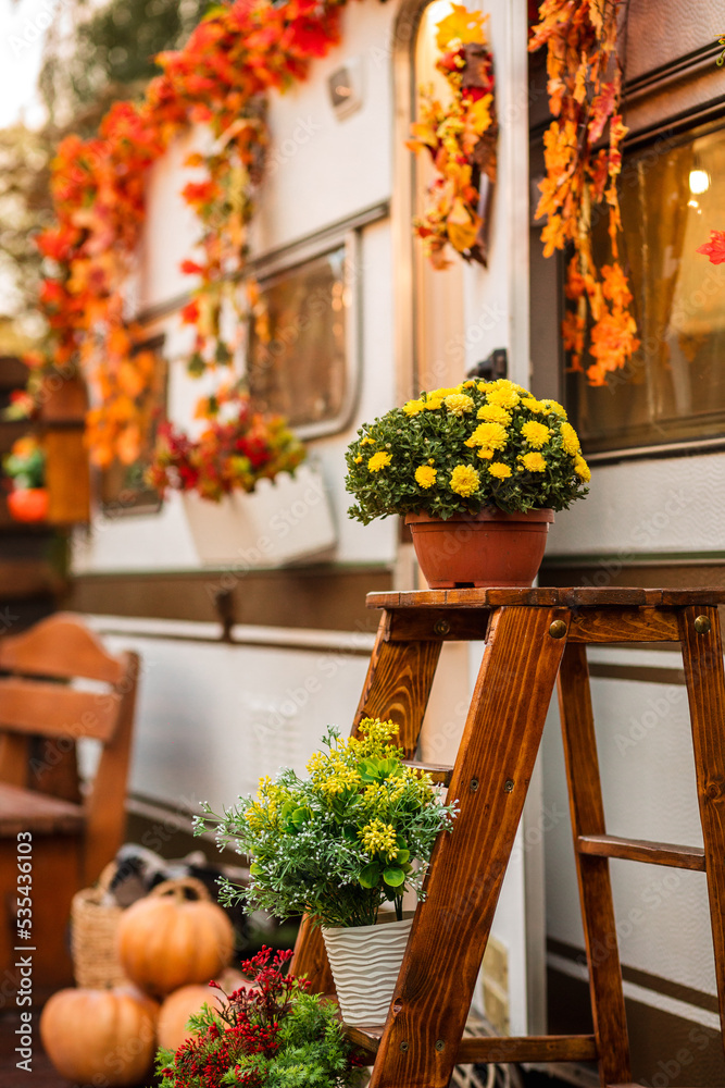 Trailer in autumn. Camping in autumn scenery. potted flowers and pumpkins