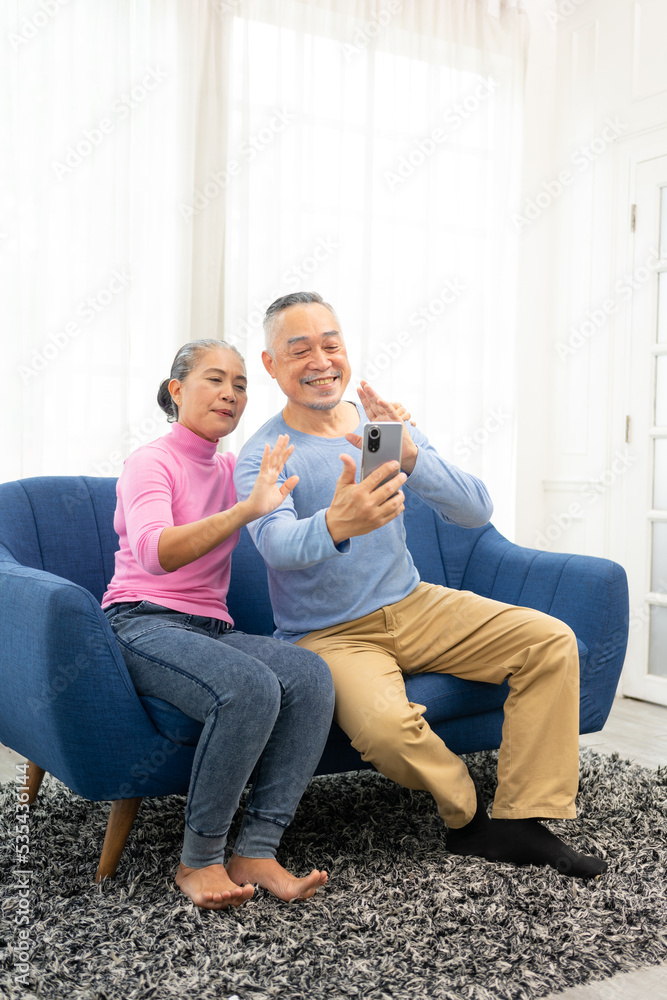 Happy smiling asian senior couple sitting on sofa and using smartphone for online video call at home living room. Smiling mature Video Call Conference talk chat online concept.