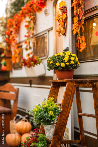 Trailer in autumn. Camping in autumn scenery. potted flowers and pumpkins