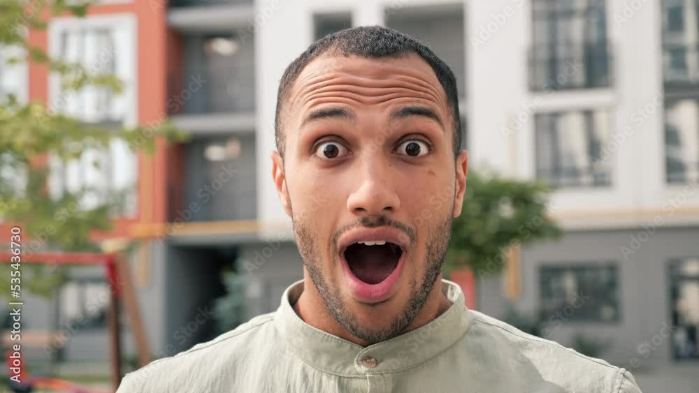 Amazed african american man shocked, saying WOW outdoor. Handsome guy wearing casual clothes surprised to camera on urban background. Male dark skinned person demonstrating surprised face expression.