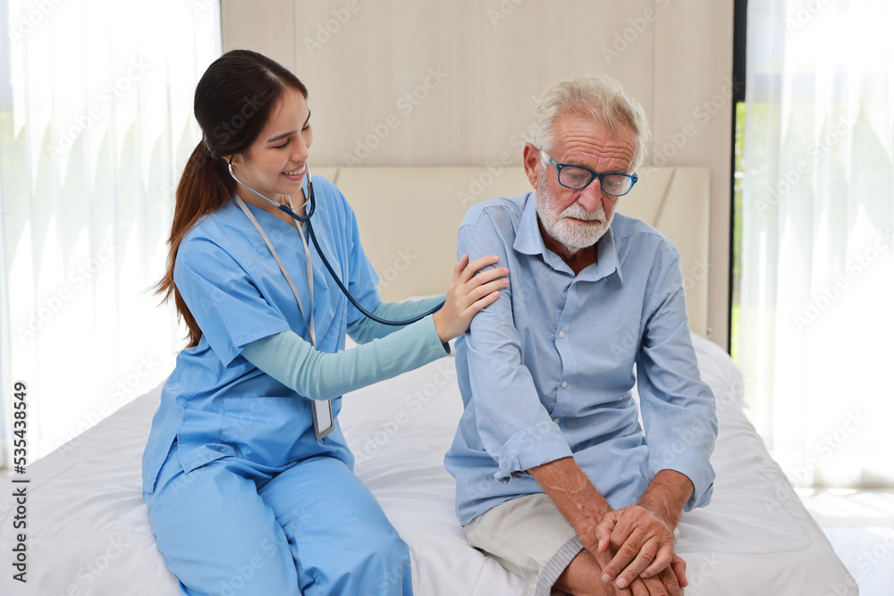 Fototapeta premium Happy caregiver examining senior elderly man patient listening heartbeat using stethoscope&nbsp;on bed at retirement house. Asian smiling nurse taking good help care and support of elder patient at house.
