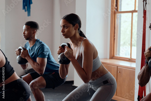 Group of determined multiracial young adults doing kettlebell squats at the gym