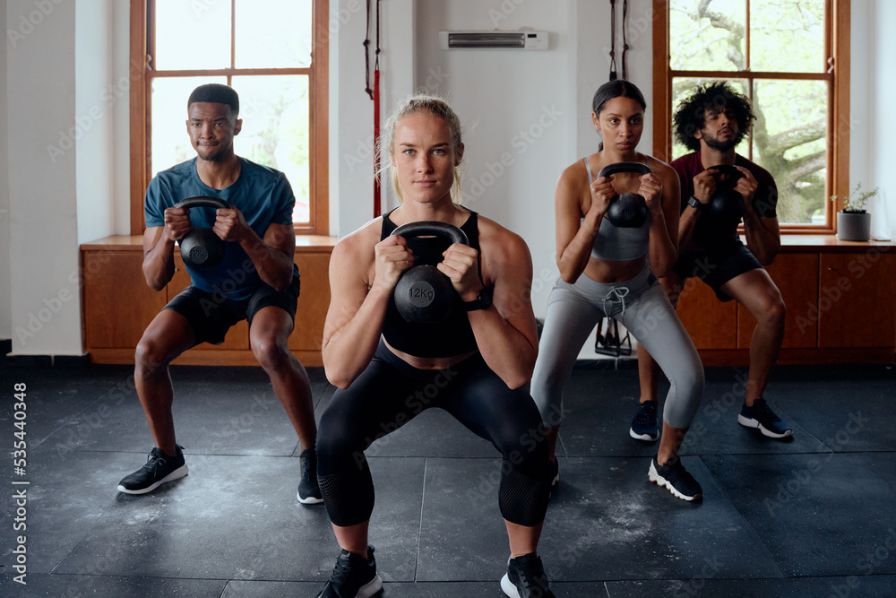 Group of fit multiracial young adults doing kettlebell squats at the gym