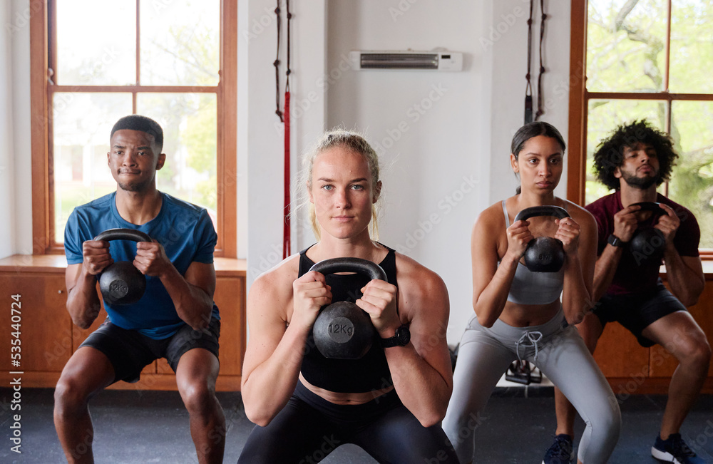 Fototapeta premium Group of resilient multiracial young adults doing kettlebell squats at the gym