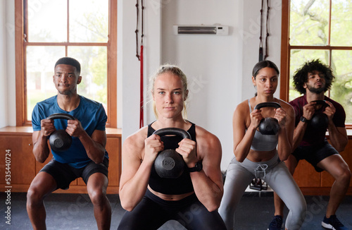 Group of resilient multiracial young adults doing kettlebell squats at the gym