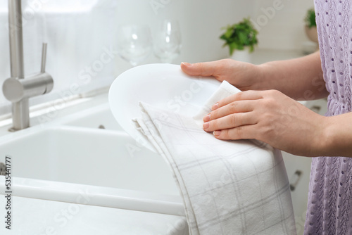 Woman wiping plate with towel near sink in kitchen, closeup