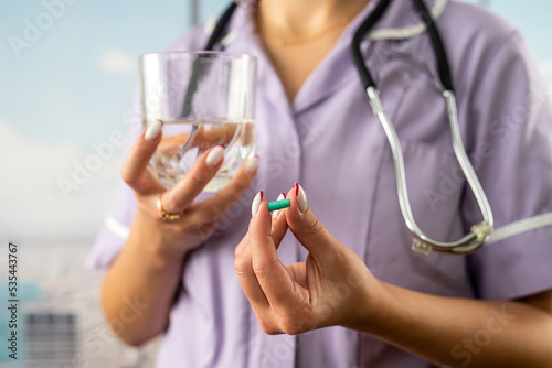 cropped photo of female doctor holding pill and glass of water in two hands in hospital. photo