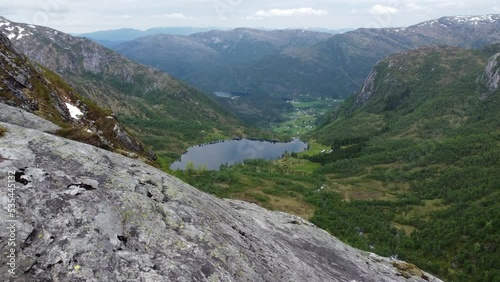 Leirovatnet freshwater lake and Eidslandet village in background is revealed from a distand mountaintop in Stamnes Vaksdal Norway - Forward moving aerial close to cliff and mountain viewpoint photo