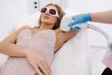 Beautician doing epilation on female's armpit in beauty center. Woman receiving laser light hair removal treatment for hairless smooth skin at cosmetology salon