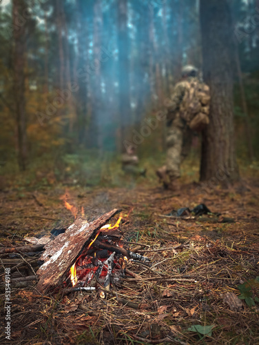 Campfire shelter in hiking time in forest with military person unfocused silhouette background scenic view vertical photography