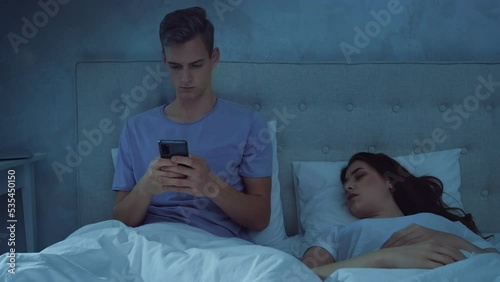 Man Chatting on Phone While Girl is Sleeping at Night. Man Using Phone in Bed. Girl Sleeping in bed. Shot on RED