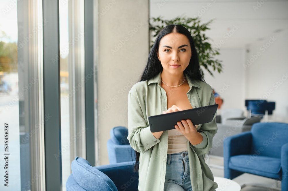 Young modern female freelancer in airport lounge or business center and works using digital tablet, creating new design project Young modern female freelancer in airport lounge or business center and works using digital tablet, creating new design project