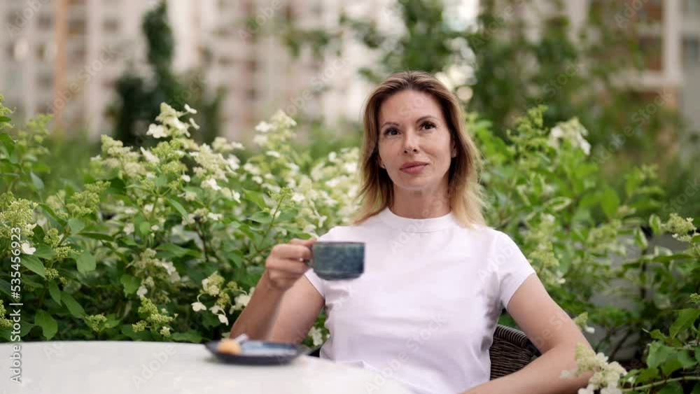 elegant middle-aged woman is enjoying coffee, drinking hot tea from cup and sitting alone elegant middle-aged woman is enjoying coffee, drinking hot tea from cup and sitting alone