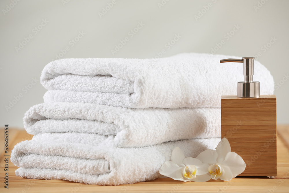 Stack of folded towels, orchid flowers and dispenser on wooden table Stack of folded towels, orchid flowers and dispenser on wooden table