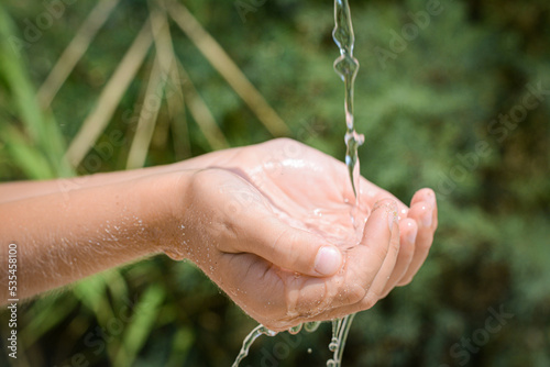 Pouring water into kid`s hands outdoors, closeup