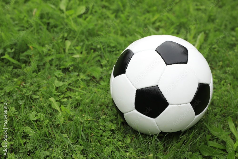 Football ball on green grass outdoors, space for text