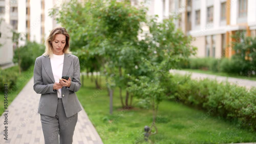 attractive lady in business suit is walking in city and using smartphone, beautiful nature of park attractive lady in business suit is walking in city and using smartphone, beautiful nature of park