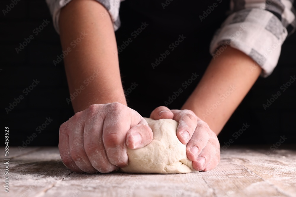 Man kneading dough at wooden table on dark background, closeup Man kneading dough at wooden table on dark background, closeup