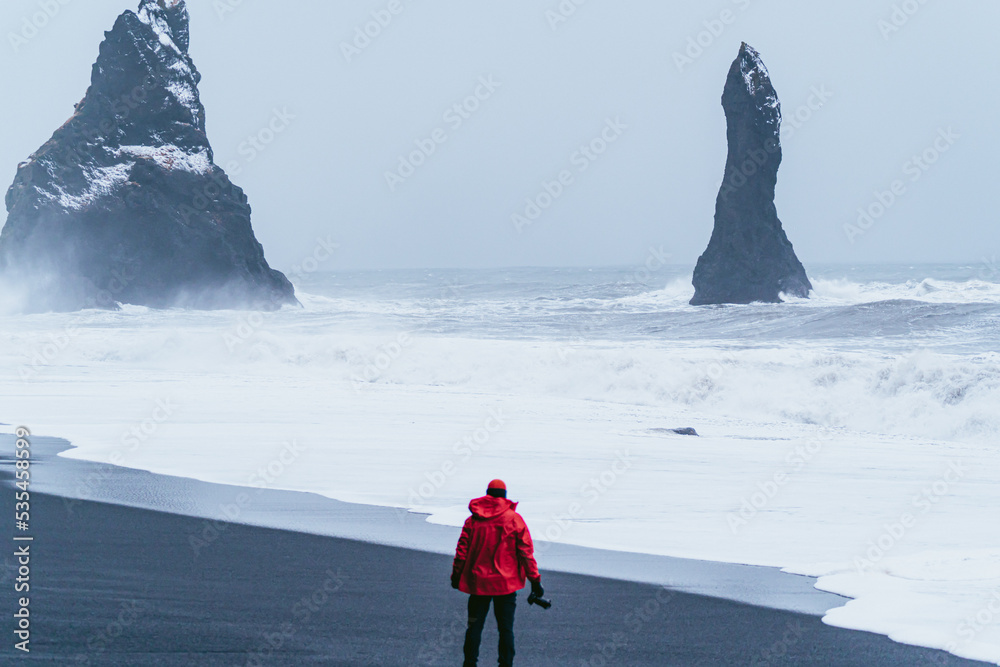photographer man on the very cold black sand beach. Big rocks.