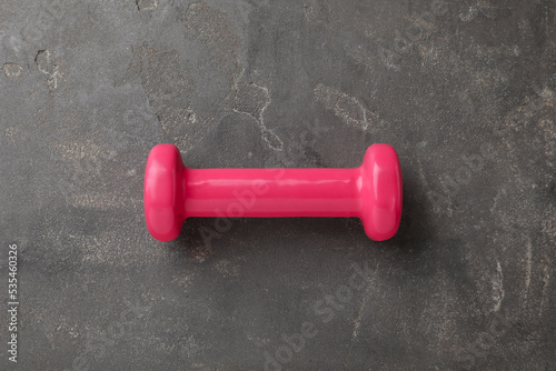 One pink dumbbell on grey table, top view