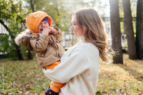 Mother and son walking in autumn park outdoor. Woman holding toddler boy on hands. Family of two