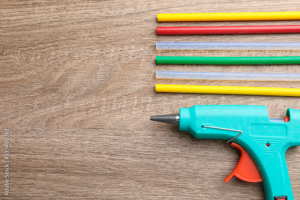 Turquoise glue gun and colorful sticks on wooden table, flat lay. Space for text