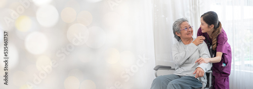 Asian young nurse taking care and talking mature female patient sitting on wheelchair in hospital. Healthcare concept, Banner cover design.