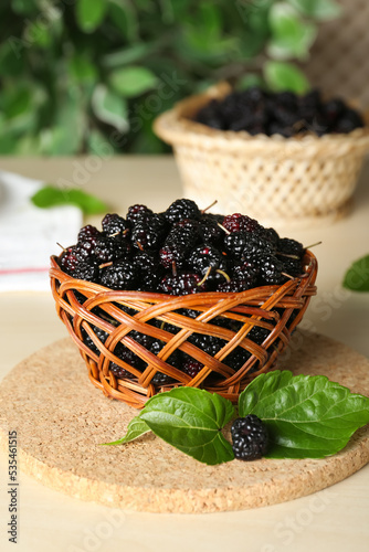 Wicker basket of delicious ripe black mulberries on white table photo