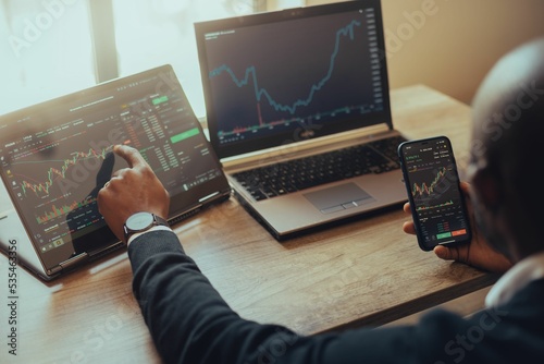 Εκτύπωση καμβά Young man holding a smartphone and laptop with online trading chart of crypto on