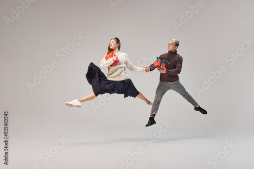 Flexible dancers, young happy couple in warm winter clothes dancing with festive gift boxes over grey background. Merry Christmas, New year, holidays, party concept