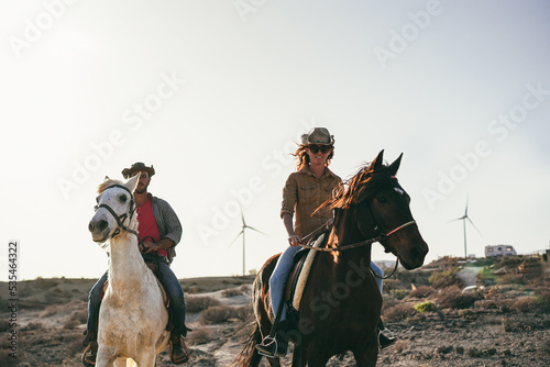 Young couple riding horses doing excursion at sunset - Soft focus on left horse face photo