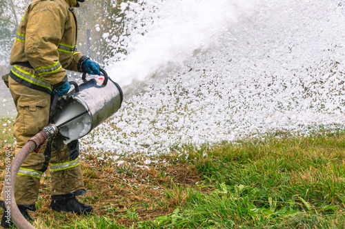 A firefighter in protective clothing extinguishes a fire by feeding foam. A firefighter extinguishes a fire with a foam generator. Foam for extinguishing the combustion of flammable liquids.
