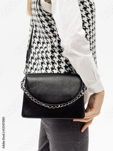 Woman with black leather shoulder bag with long strap on white background. Office style. Vertical