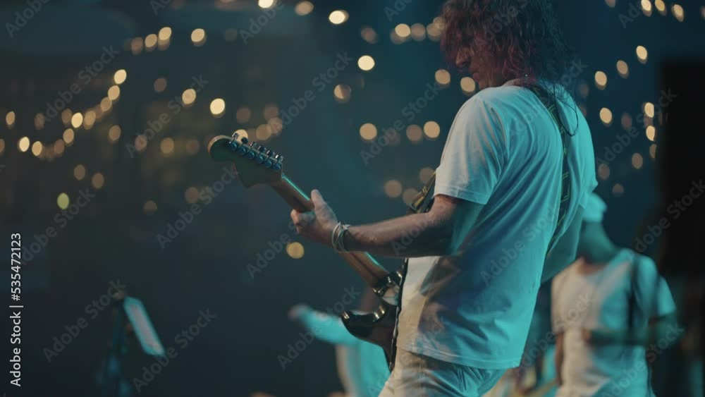 hard rock gig, male musician is playing electric guitar on stage and moving by music rhythm