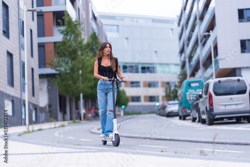 A young brunette woman moving in the city with an electric scooter, along the bike lane